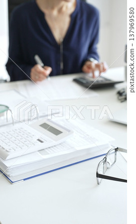 Professional analyzing financial data, writing notes near laptop, magnifying glass, documents, binders on workplace desk. Audit and taxes concept Professional analyzing financial data, writing notes near laptop, magnifying glass, documents, binders on workplace desk. Audit and taxes concept 137969580