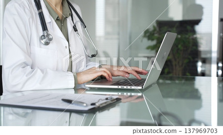 Adult doctor woman working on laptop, typing during online consultation, providing medical care and remote healthcare service. Medicine, health care and science concept Adult doctor woman working on laptop, typing during online consultation, providing medical care and remote healthcare service. Medicine, health care and science concept 137969703