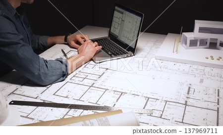 Architect feeling frustrated and stressed, working late on blueprints and building plans, designing a new house with a laptop and architectural model on a desk Architect feeling frustrated and stressed, working late on blueprints and building plans, designing a new house with a laptop and architectural model on a desk 137969711