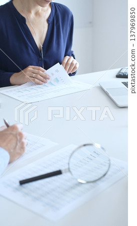 Magnifying glass over financial documents near blue folders full of papers, male accountant is analyzing reports and documents at the background. Audit and taxes in business 137969850