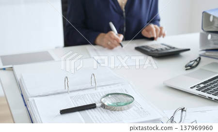 Professional analyzing financial data, writing notes near laptop, magnifying glass, documents, binders on workplace desk. Audit and taxes concept Professional analyzing financial data, writing notes near laptop, magnifying glass, documents, binders on workplace desk. Audit and taxes concept 137969960