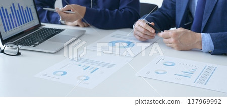 Businessman and businesswoman are analyzing financial data on a laptop and printed documents, pointing at charts and graphs during a meeting in bright office. Business people and finance concept Businessman and businesswoman are analyzing financial data on a laptop and printed documents, pointing at charts and graphs during a meeting in bright office. Business people and finance concept 137969992