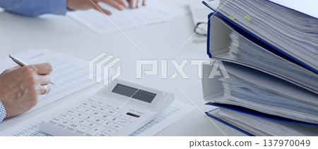 Two professional accountants analyzing financial documents and using a calculator with a laptop in a bright office. Audit and taxes in business Two professional accountants analyzing financial documents and using a calculator with a laptop in a bright office. Audit and taxes in business 137970049