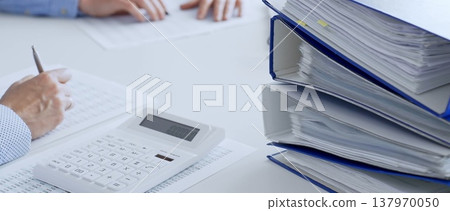 Two accountants collaborating in a bright office, analyzing financial documents and using a calculator with a laptop displaying charts. Audit and taxes in business Two accountants collaborating in a bright office, analyzing financial documents and using a calculator with a laptop displaying charts. Audit and taxes in business 137970050