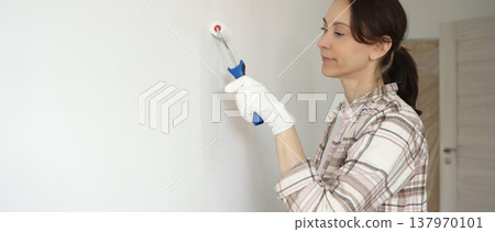 Woman wearing protective gloves painting white wall with small paint roller, updating interior and giving room clean, modern look during home renovation project Woman wearing protective gloves painting white wall with small paint roller, updating interior and giving room clean, modern look during home renovation project 137970101