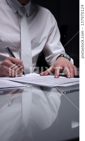 Business man signing a contract late in the office, closing a deal, or completing legal paperwork at deep night. Audit and overworking concepts Business man signing a contract late in the office, closing a deal, or completing legal paperwork at deep night. Audit and overworking concepts 137970124