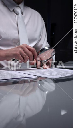 Business person examining a document using a magnifying glass, focusing on fine print and terms in a legal agreement, working late. Audit and overworking concepts 137970139