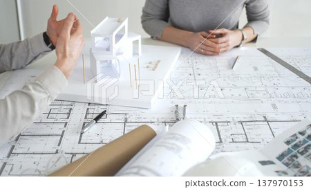 Architects discussing modern building design with 3d model and blueprints during planning meeting focused on innovation, teamwork and sustainable construction solutions, close up Architects discussing modern building design with 3d model and blueprints during planning meeting focused on innovation, teamwork and sustainable construction solutions, close up 137970153