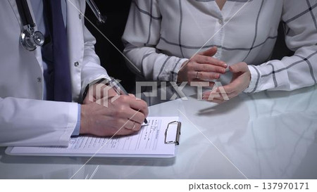 Physician consulting with patient, filling out medical records during a healthcare check up, discussing health concerns and providing treatment information. Overwork in medicine Physician consulting with patient, filling out medical records during a healthcare check up, discussing health concerns and providing treatment information. Overwork in medicine 137970171
