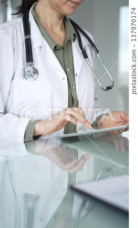 Doctor woman accessing patient data on digital tablet, managing healthcare records in modern medical office. Medicine, health care and science concept Doctor woman accessing patient data on digital tablet, managing healthcare records in modern medical office. Medicine, health care and science concept 137970174