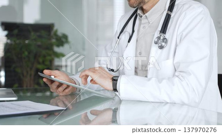 Doctor man in white coat using tablet, working with patient medical records and digital health information in clinic. Medicine, healthcare and science concept Doctor man in white coat using tablet, working with patient medical records and digital health information in clinic. Medicine, healthcare and science concept 137970276