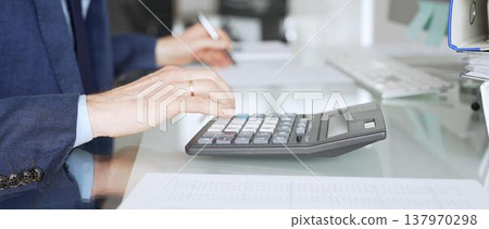 Accountant's hands calculating and writing on financial documents at a desk, managing budgets, reports and tax paperwork. Audit and taxes in business Accountant's hands calculating and writing on financial documents at a desk, managing budgets, reports and tax paperwork. Audit and taxes in business 137970298