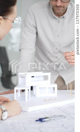 Architects are discussing building plans, using a compass over blueprints while collaborating on a new construction project in an office, emphasizing design, planning, and teamwork, close up 137970308