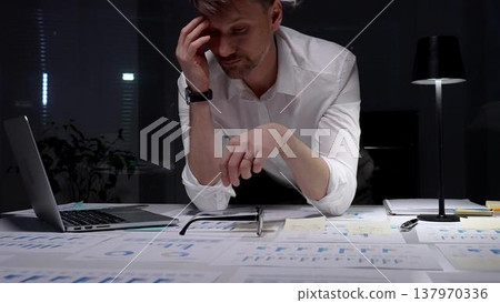 Stressed businessman suffering from overwhelming burnout and work overload, working late into the night, feeling frustrated with deadline pressure in a dark office environment 137970336