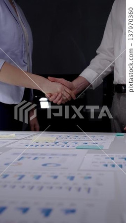 Business partners shaking hands over desk with financial documents, concluding deal, showing success in collaboration, partnership, and agreement during a late meeting at office Business partners shaking hands over desk with financial documents, concluding deal, showing success in collaboration, partnership, and agreement during a late meeting at office 137970360