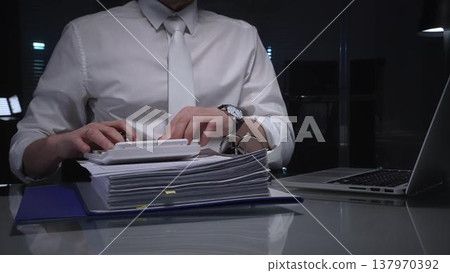 Businessman carefully examining financial documents, focusing on research and audit in a dark office. Audit and taxes in business Businessman carefully examining financial documents, focusing on research and audit in a dark office. Audit and taxes in business 137970392