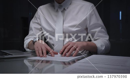 Man in white shirt reviewing legal documents, checking details of a contract with a magnifying glass on a dimly lit desk. Audit, business and overworking concepts 137970398