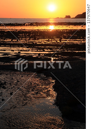A shallow beach bathed in the red glow of the setting sun. A shallow beach bathed in the red glow of the setting sun. 137970647