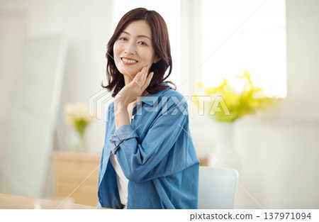 A middle-aged woman smiles at the camera in her living room. A middle-aged woman smiles at the camera in her living room. 137971094