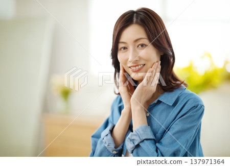 A middle-aged woman smiles at the camera in her living room. A middle-aged woman smiles at the camera in her living room. 137971364