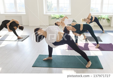 Yoga group holding bound side angle pose together in serene sunlit studio Yoga group holding bound side angle pose together in serene sunlit studio 137971727