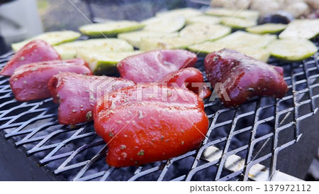 Vegetables roasting on home grill over open heat at summer day. Smoke rises gently as meal cook developing lightly charred surface. The focus on grilling process, texture and appetizing appearance 137972112