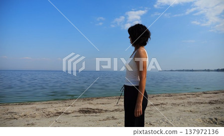 Happy adult woman going on sandy beach near shoreline at sunny day. Beautiful lady walking on seashore with calm waves at background. Concept of summer vacation or holiday. Slow motion Happy adult woman going on sandy beach near shoreline at sunny day. Beautiful lady walking on seashore with calm waves at background. Concept of summer vacation or holiday. Slow motion 137972136