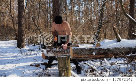 Shirtless man sawing a log in sunny winter forest. Strong guy working with saw in snowy woodland. The scene highlights human effort and outdoor activity in cold conditions. Slow mo Shirtless man sawing a log in sunny winter forest. Strong guy working with saw in snowy woodland. The scene highlights human effort and outdoor activity in cold conditions. Slow mo 137972142