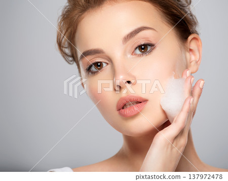 Girl moistens her face. Woman with soap foam street. Beautiful face of young caucasian woman with perfect healthy skin, isolated. Pretty white model caring of face. Skin care concept. Girl moistens her face. Woman with soap foam street. Beautiful face of young caucasian woman with perfect healthy skin, isolated. Pretty white model caring of face. Skin care concept. 137972478