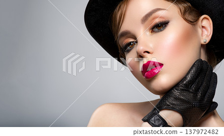 Art portrait of beautiful young woman with orange makeup in a black hat. Closeup face of a sexy girl with red lipstick on lips. Stylish fashion portrait. Attractive model with a black gloves at Art portrait of beautiful young woman with orange makeup in a black hat. Closeup face of a sexy girl with red lipstick on lips. Stylish fashion portrait. Attractive model with a black gloves at 137972482
