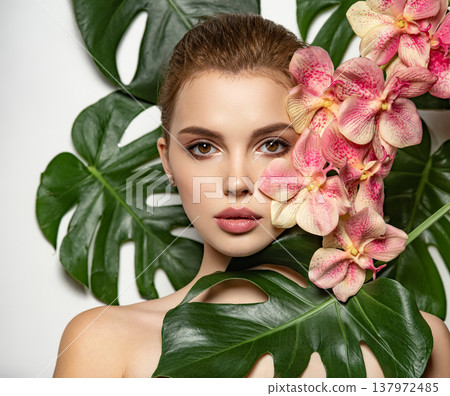Pretty girl in Skin care beauty treatments concept.  Beautiful woman with green leave near face and body. Closeup girl's face with green leave. Model with pink tropical orchid near face. Brown 137972485