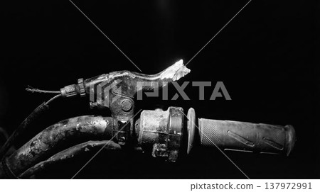Close-up of damaged motorbike control, gritty industrial aesthetic. Worn metal texture on a dark background. Close-up of damaged motorbike control, gritty industrial aesthetic. Worn metal texture on a dark background. 137972991