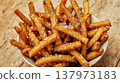 A bowl of crispy golden French fries sprinkled with salt on a rustic wooden table. The fries are evenly cut and have a crunchy texture. 137973183