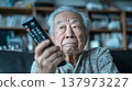 Image of a senior citizen holding a remote control 137973227