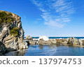A rocky coastline with waves crashing against the blue sky. 137974753