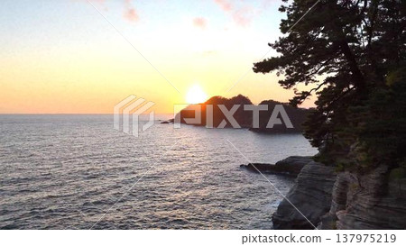 A beautiful sunset over Dogashima. The setting sun sinking behind the island and the silhouettes of pine trees (aerial view). 137975219
