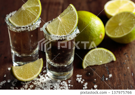 Tequila with salt and lime slices on an old wooden table. Tequila with salt and lime slices on an old wooden table. 137975766
