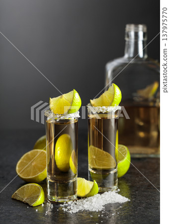 Tequila shots with salt and lime slices on a black stone table. Tequila shots with salt and lime slices on a black stone table. 137975770