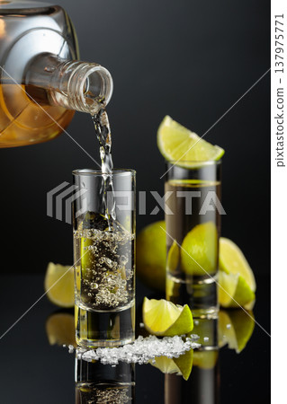 Tequila shots with salt and lime slices on a black reflective background. 137975771