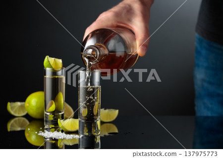 Tequila shots with salt and lime slices on a black reflective background. Tequila shots with salt and lime slices on a black reflective background. 137975773