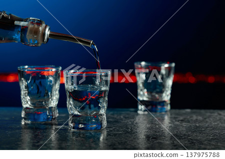 Vodka is poured into a shot glasses. Vodka is poured into a shot glasses. 137975788
