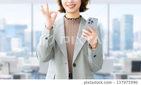 一位微笑的女人/女商人拿著智慧型手機,做出「OK」的姿勢 一位微笑的女人/女商人拿著智慧型手機,做出「OK」的姿勢 137975996