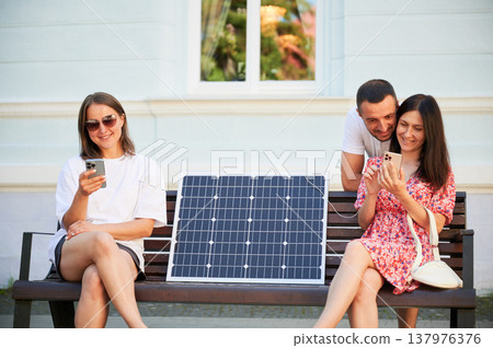 People using smartphone connected to solar panel. Integration of sustainable renewable energy into everyday life, demonstrating practical use of solar power for charging devices. 137976376