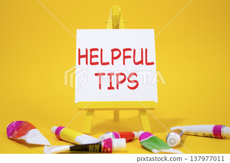 Helpful tips symbol. Wooden blocks with words Helpful tips. Beautiful yellow background with paints and easel. Business and Helpful tips concept. Copy space. 137977011