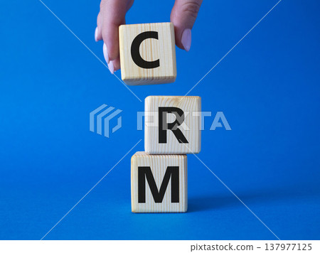 CRM - Customer relationship management symbol. Concept word CRM on wooden cubes. Businessman hand. Beautiful blue background. Business and CRM concept. Copy space. 137977125