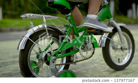 Three year old boy rear view riding green kids bicycle on path in park Three year old boy rear view riding green kids bicycle on path in park 137977167