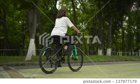 Woman riding bicycle in park rear view 4k 137977179