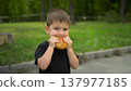 Little boy eats cheeseburger in park and looks at camera portrait shot 4k 137977185