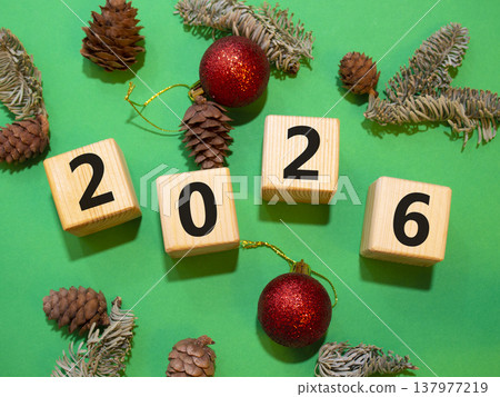 2026 New Year symbol. Wooden cubes with words 2026. Beautiful green background with Christmas balls and pine cones. Copy space. Business and 2026 happy new year concept 2026 New Year symbol. Wooden cubes with words 2026. Beautiful green background with Christmas balls and pine cones. Copy space. Business and 2026 happy new year concept 137977219