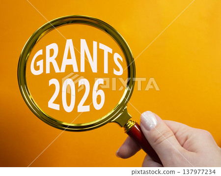 Grants 2026 symbol. Magnifying Glass with words Grants 2026. Businessman hand. Beautiful orange background. Business and Grants 2026 concept. Copy space. Grants 2026 symbol. Magnifying Glass with words Grants 2026. Businessman hand. Beautiful orange background. Business and Grants 2026 concept. Copy space. 137977234